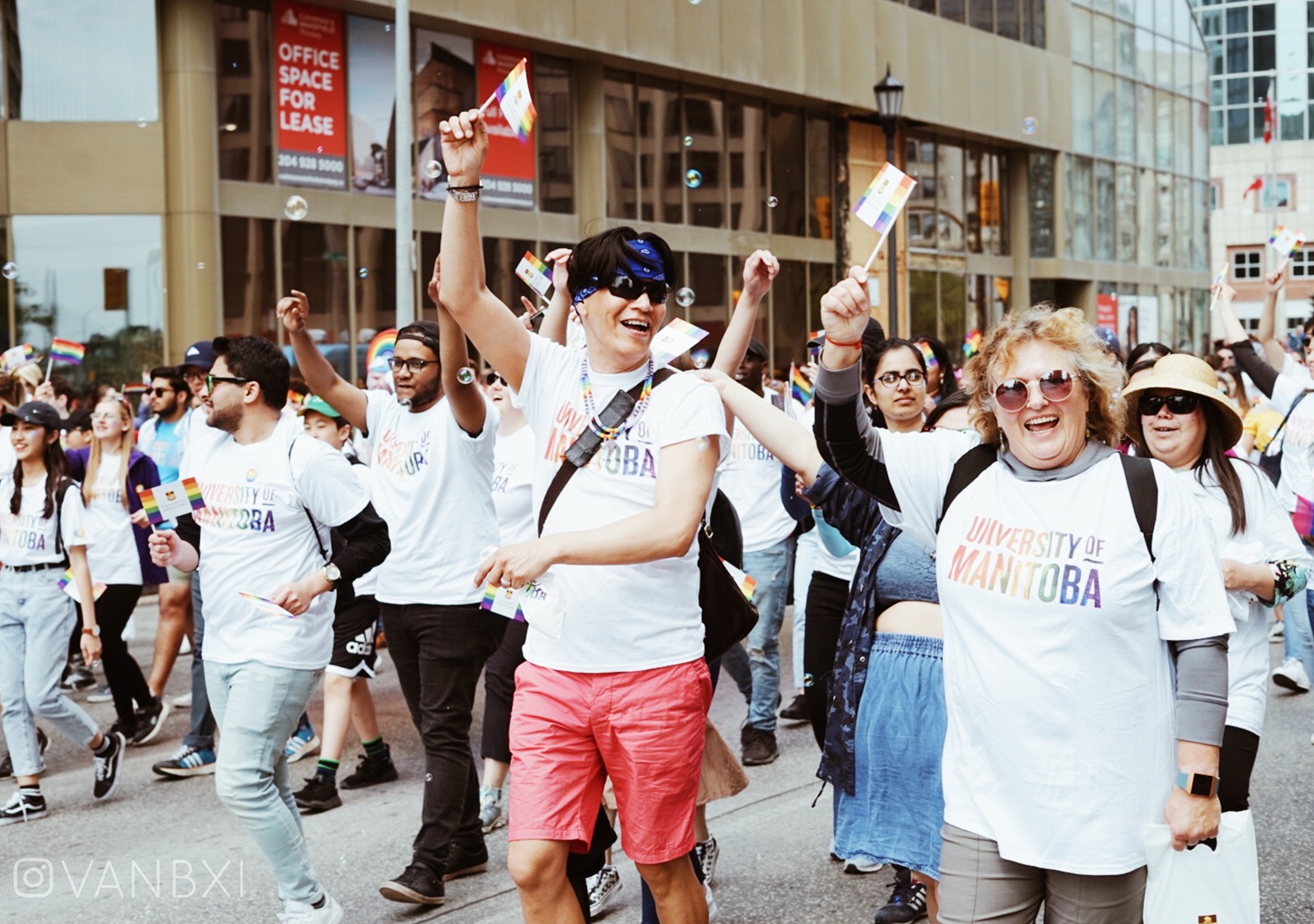 A group of people representing the University of Manitoba holding pride flags and marching in the Pride parade.