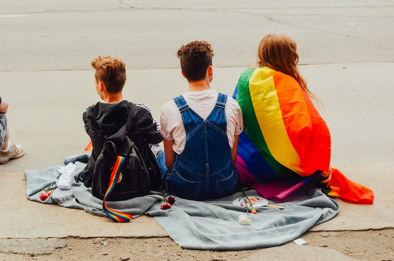 three kids seating on the floor holding a pride flag